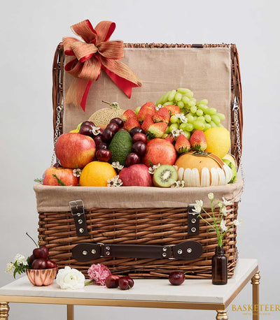 Elegant wicker fruit gift basket overflowing with fresh apples, grapes, strawberries, and seasonal produce with red and gold