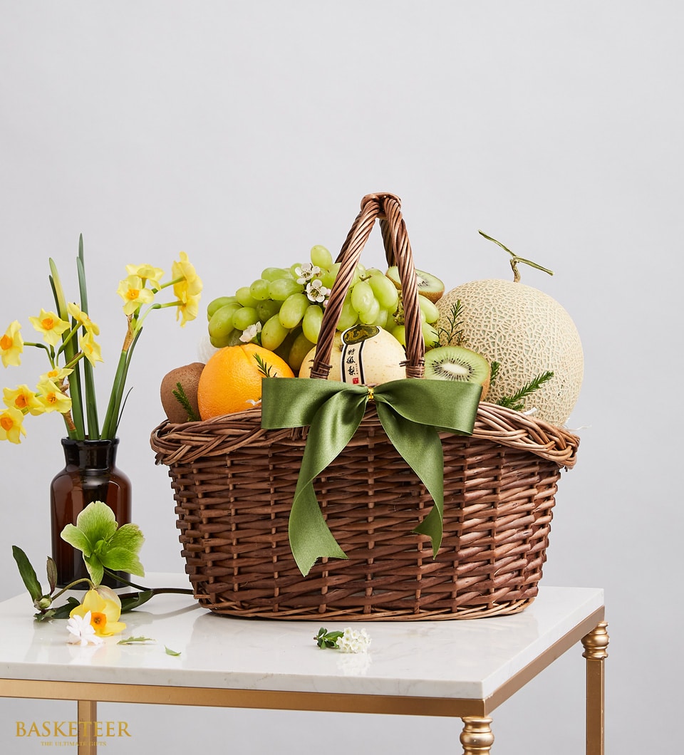 Luxury fruit basket with green grapes, cantaloupe, oranges, kiwis, and pear in wicker with olive ribbon