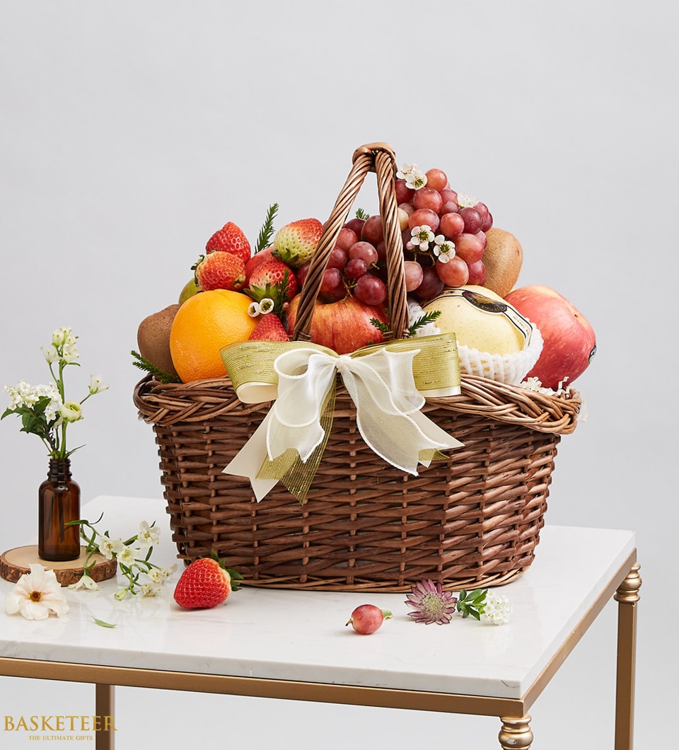 Luxury fresh fruit basket with grapes, strawberries, oranges, and apples in dark woven wicker with cream ribbon bow