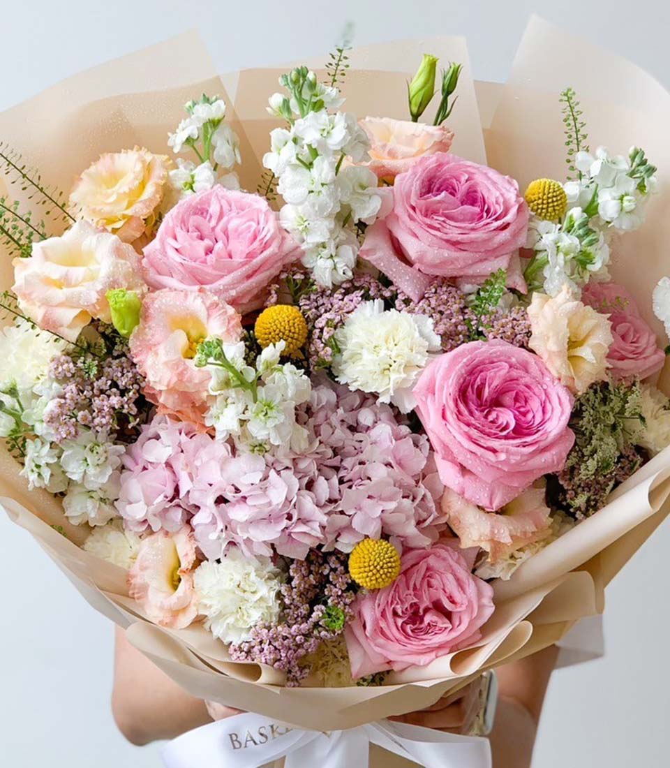 Vibrant mixed flower bouquet with pink garden roses, white stock, hydrangeas, and yellow craspedia in kraft paper wrap