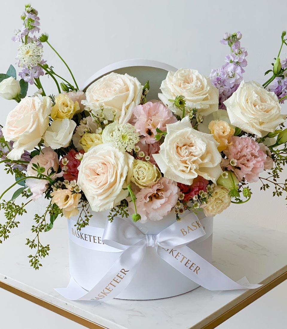 Pastel roses and seasonal blooms in cream white hatbox with satin ribbon, fresh flower gift for birthdays
