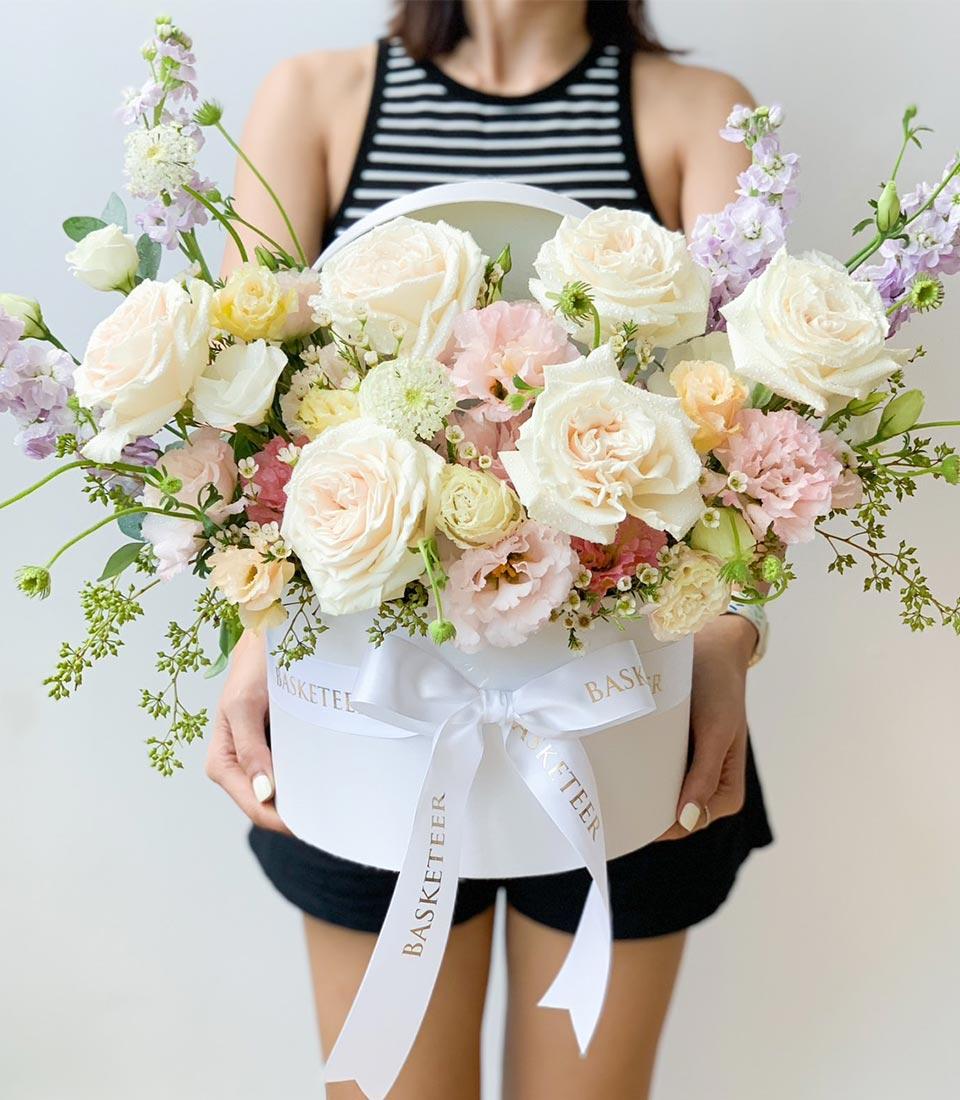 Delicate pastel roses and lisianthus in luxury white round gift box with gold ribbon