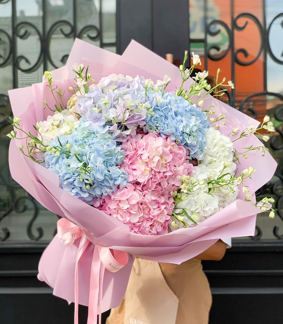 Vibrant hydrangea bouquet in blue, pink, and purple with light pink wrapping and satin ribbon bow