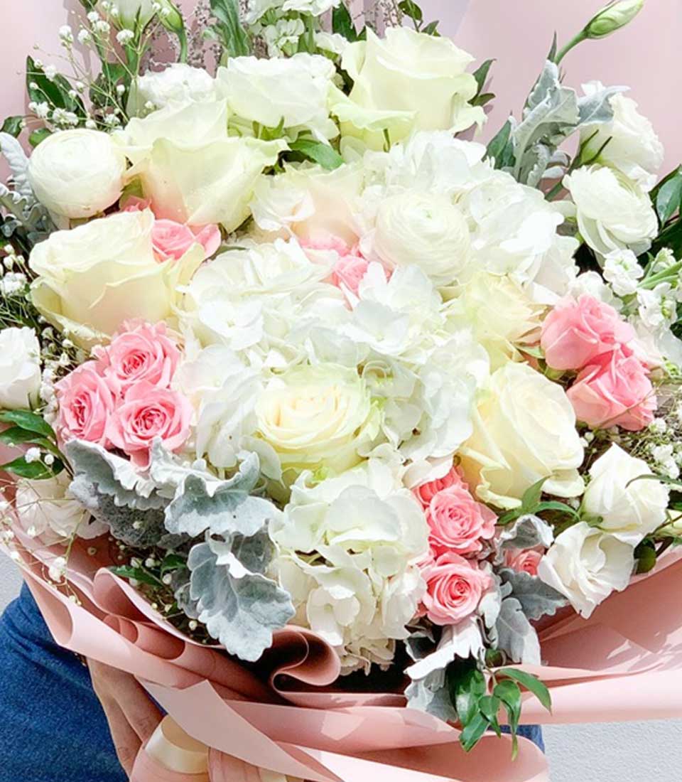 Luxe bouquet of white and pale yellow roses, pink spray roses, and hydrangeas with baby's breath in soft pink wrapping