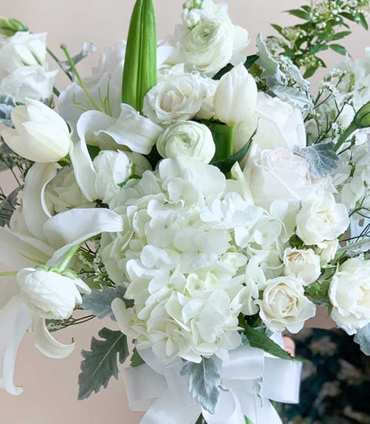 Lush white hydrangea, lily, and rose bouquet with green foliage and ribbon bow for birthday celebrations