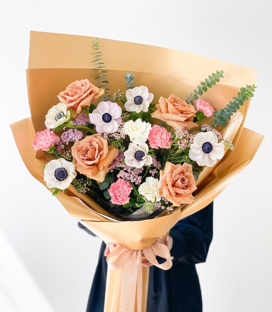 Peach anemone bouquet with roses and carnations wrapped in golden-brown paper with satin ribbon