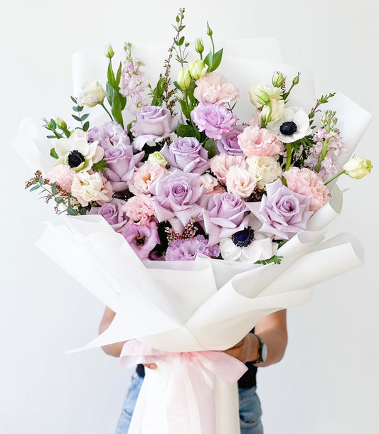 Lavender and pink rose bouquet with white anemones, lisianthus, and carnations in white paper wrapping