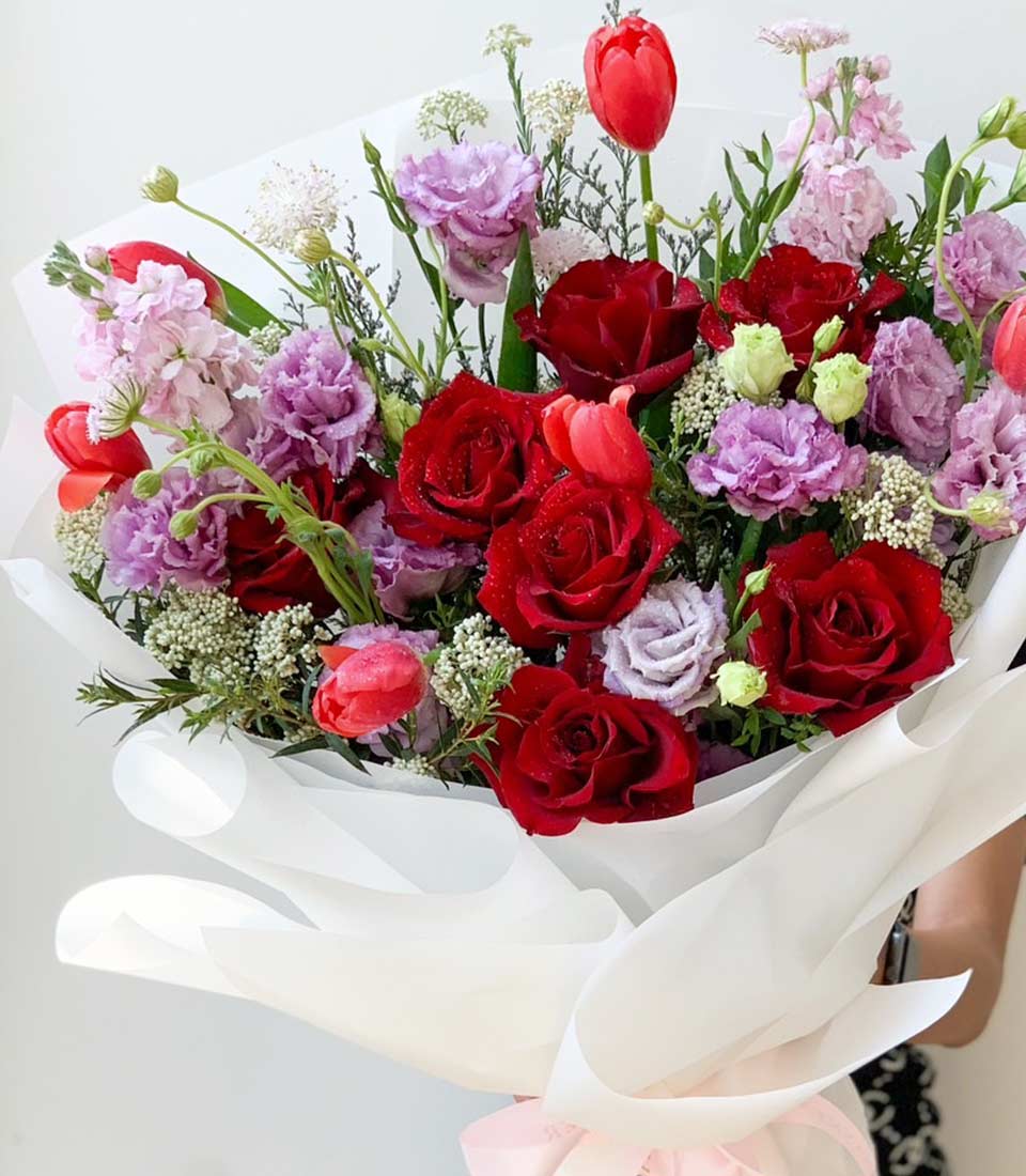 Romantic red roses, tulips, and lisianthus bouquet with pink ribbon and white wrapping