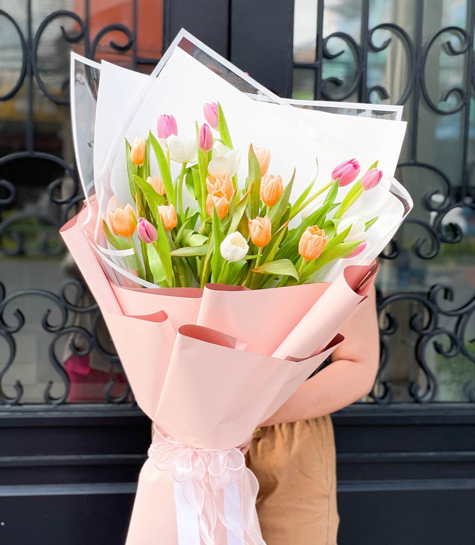 Fresh spring tulips in white, pink, and peach wrapped in soft pink paper with ribbon bow