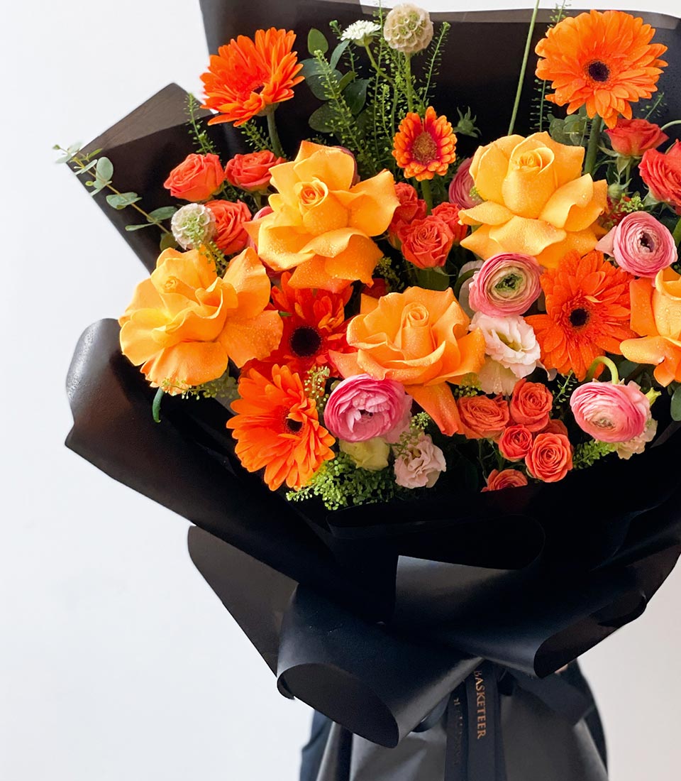 Vibrant orange and pink fresh rose bouquet with gerbera daisies and ranunculus, black wrapped