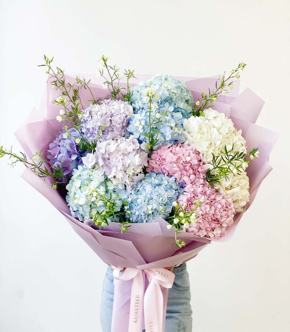 Pastel hydrangea symphony bouquet with blue, purple, pink and white blooms, wrapped in lavender paper with pink ribbon