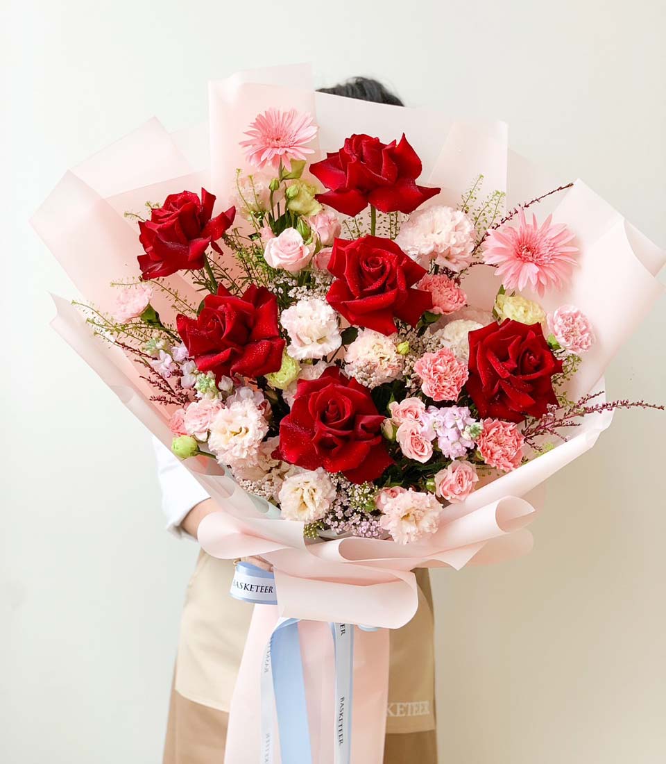 Luxe red rose bouquet with pink gerberas, carnations and cream blooms, wrapped in soft pink paper