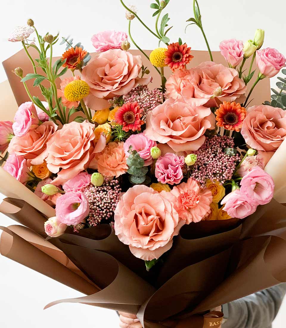 Pastel peach and pink rose bouquet with yellow craspedia and gerbera accents, wrapped in cream and brown paper