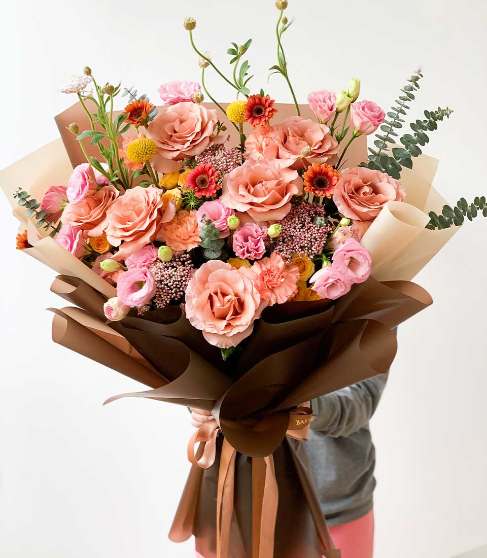 Pastel peach and pink rose bouquet with carnations and lisianthus, wrapped in kraft paper with satin ribbon
