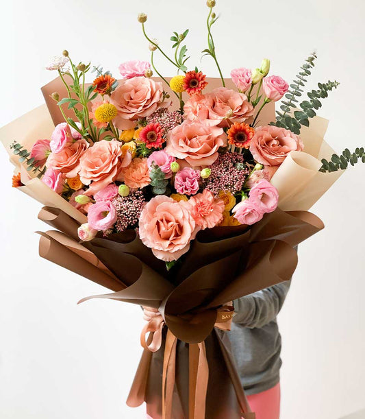 Pastel peach and pink rose bouquet with carnations and lisianthus, wrapped in kraft paper with satin ribbon