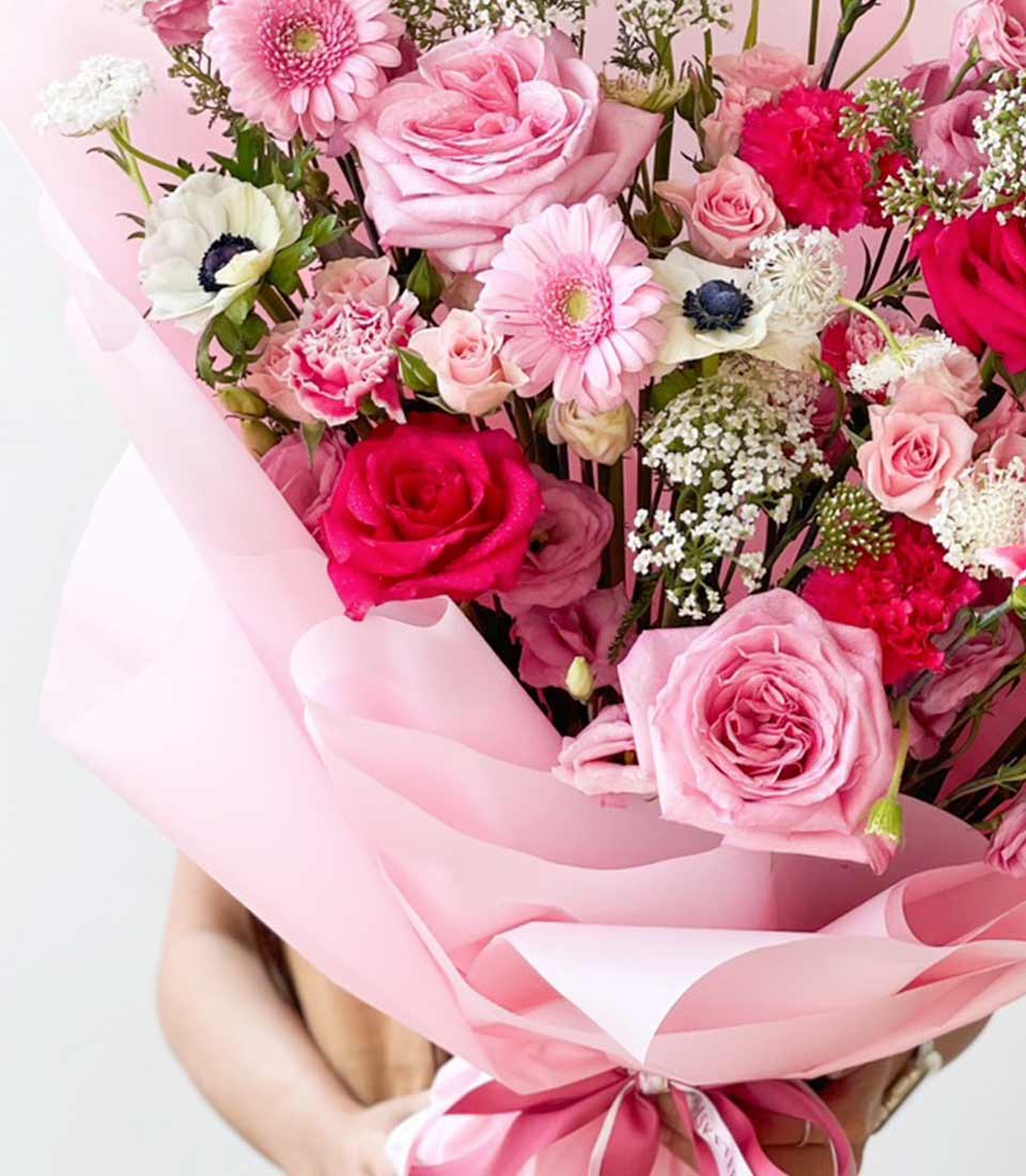 Vibrant pink and white fresh flower bouquet with roses, anemones, and gerbera daisies wrapped in light pink paper