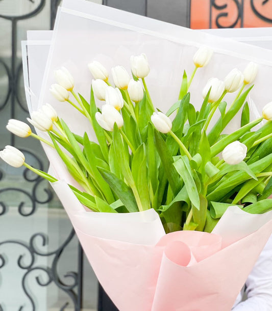 White tulip bouquet with fresh green stems in soft pink wrapping