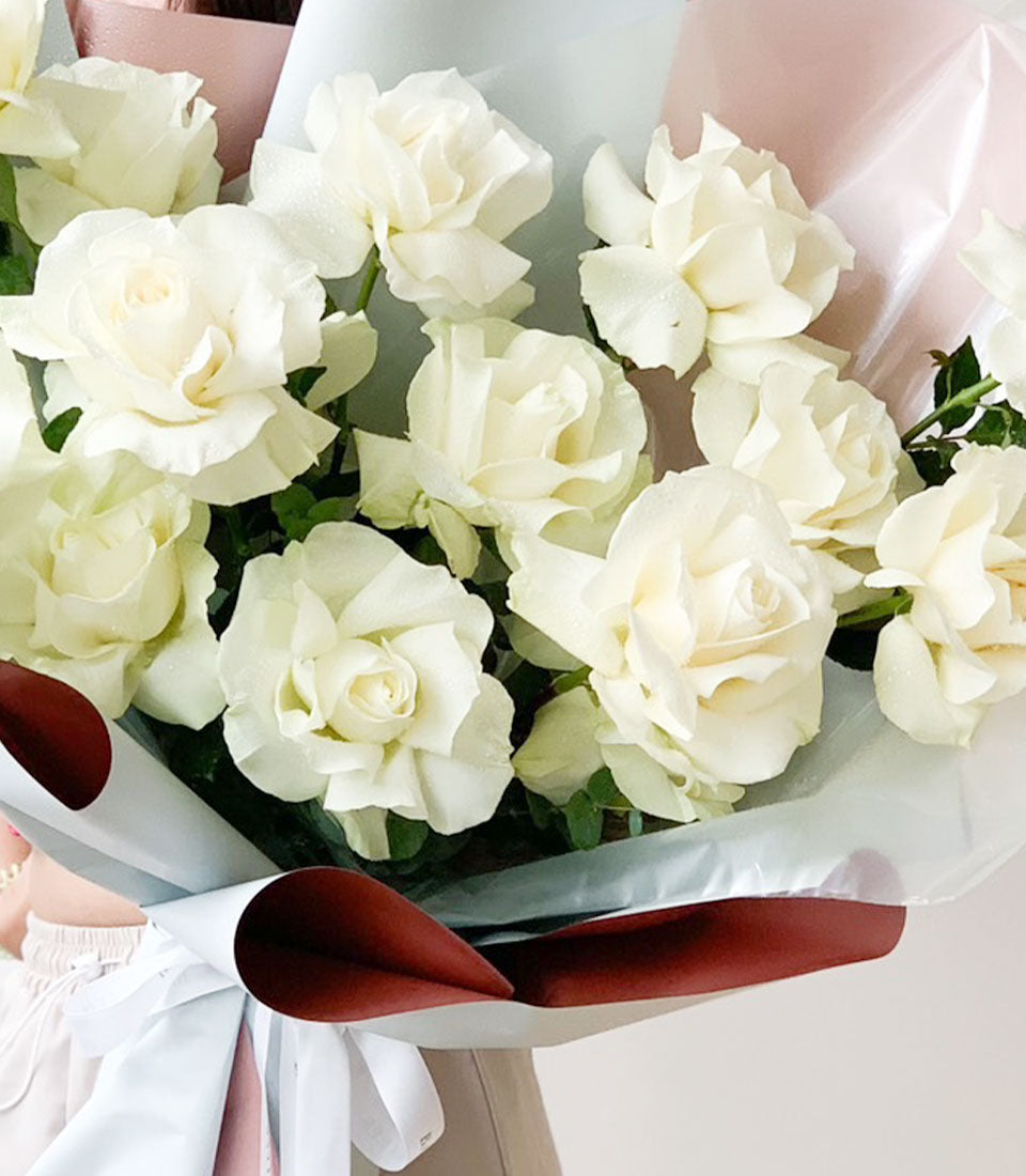 Pure white rose bouquet with fresh petals, wrapped in soft pink and mint paper with white ribbon bow