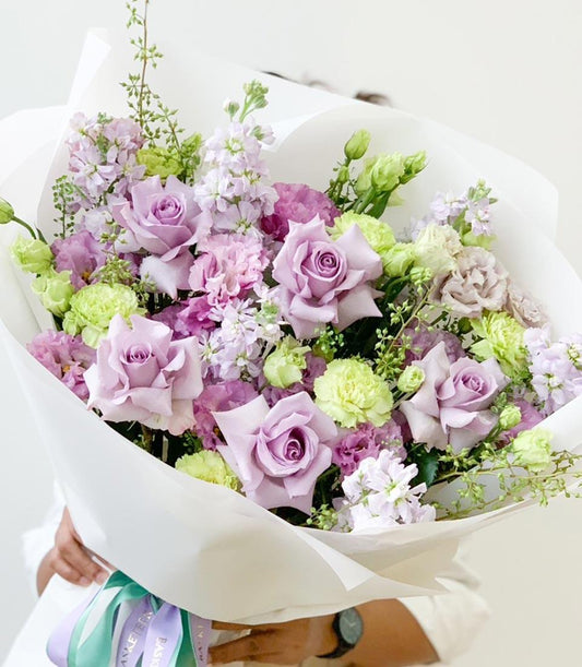 Lavender rose bouquet with carnations and green foliage wrapped in white paper with ribbon