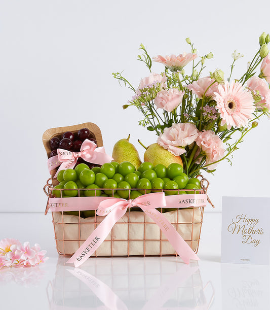 Rose gold wire basket with fresh fruit, pink flowers, and pink satin ribbon for Mother's Day gifting
