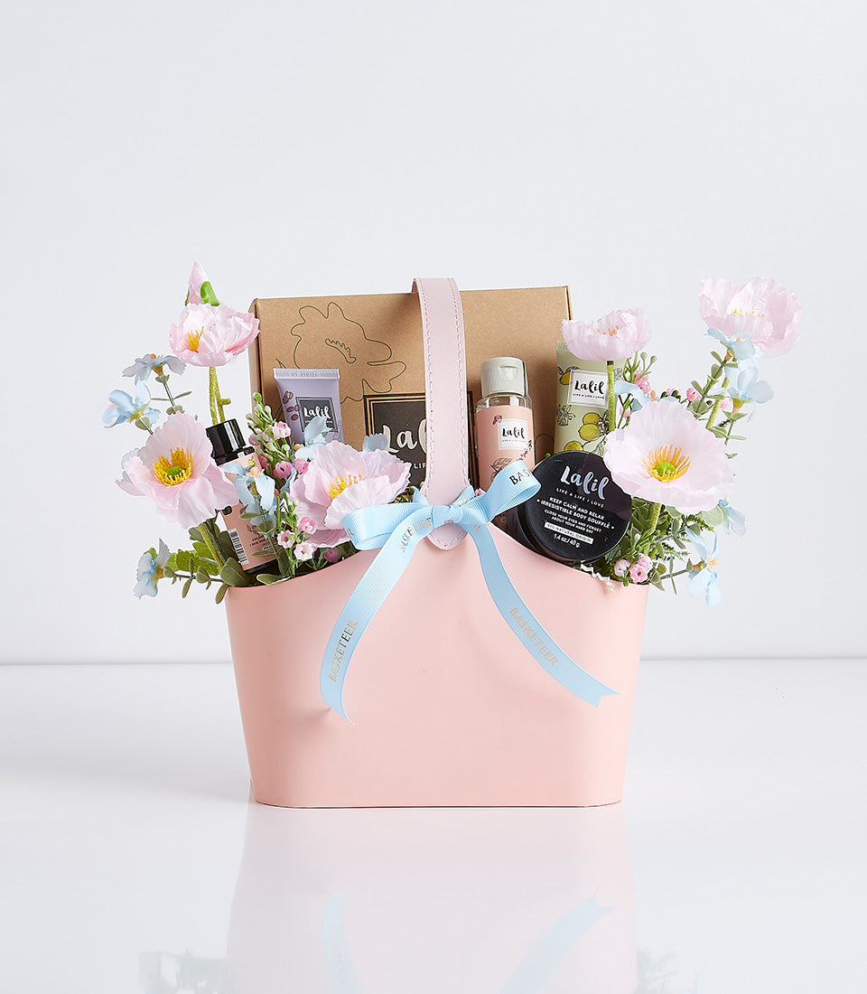 Light pink spa gift basket with fresh flowers, aromatherapy products, and blue ribbon for Mother's Day