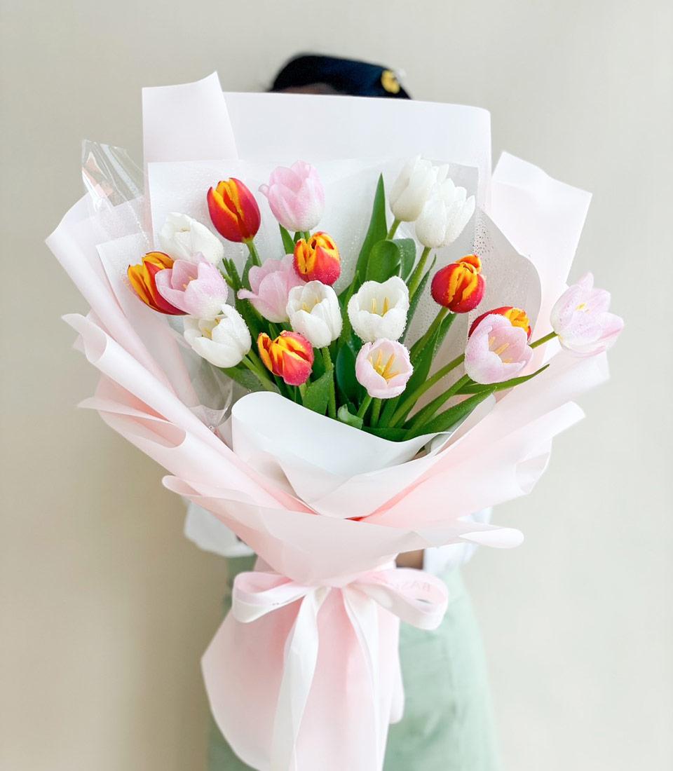Vibrant mixed tulip bouquet in white, pink, and red-orange with pink tissue wrap and ribbon bow