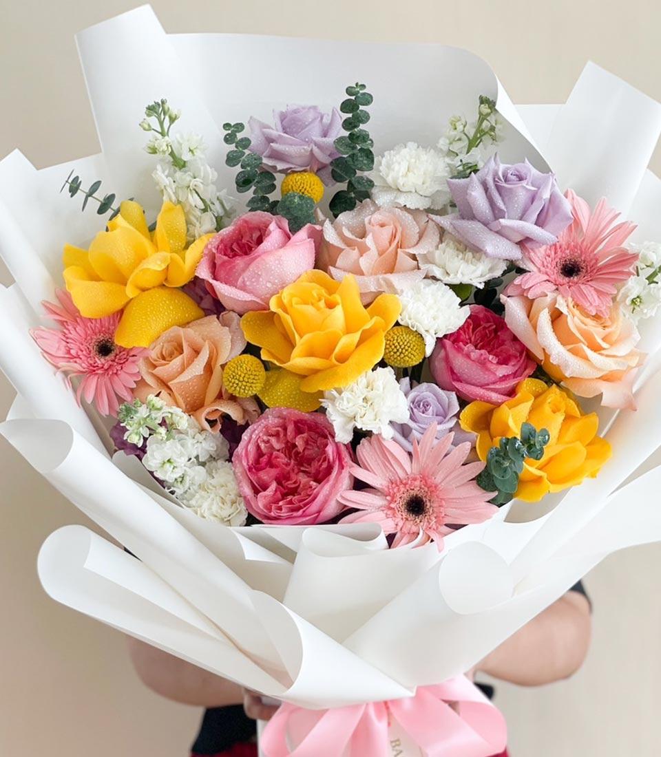Vibrant pastel flower bouquet with yellow roses, pink gerbera daisies, and eucalyptus in white paper wrap