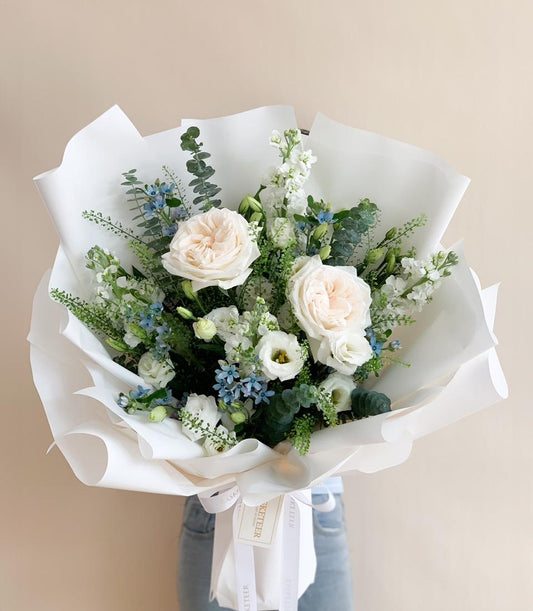 Pink garden roses, white snapdragons, and blue delphinium fresh flower bouquet wrapped in white paper