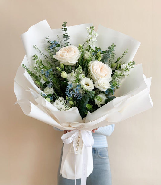 Elegant fresh flower bouquet with white and pale pink roses, lisianthus, and eucalyptus wrapped in white paper