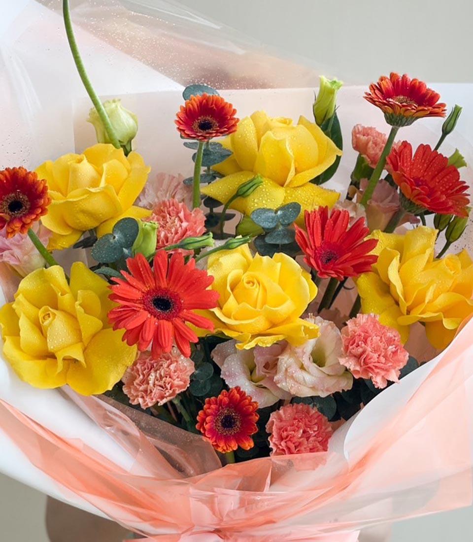 Vibrant fresh rose bouquet with yellow roses, red gerberas, and pink carnations wrapped in peach cellophane