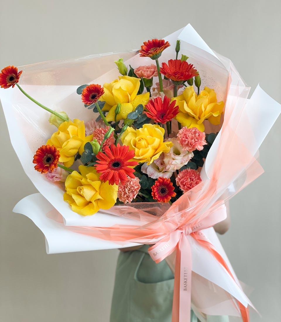 Vibrant yellow roses and red gerberas with pink carnations, wrapped in peach paper and satin ribbon