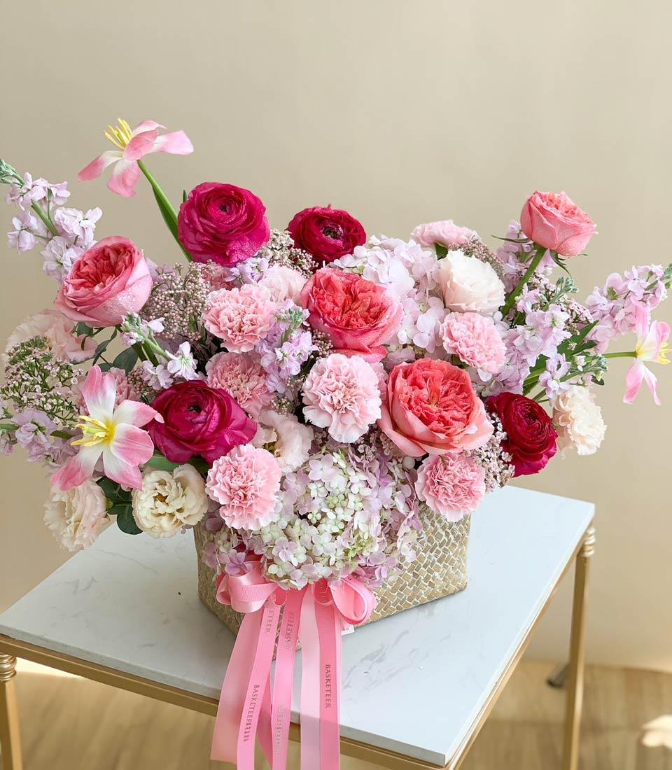 Pink rose and ranunculus woven basket arrangement with fuchsia hydrangeas and tulips for celebrations