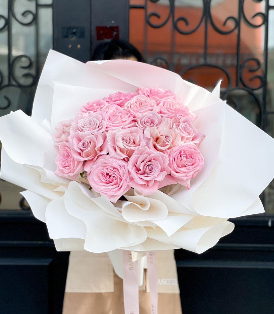 Blushing pink rose bouquet with frosted finish, wrapped in white paper and silk ribbon