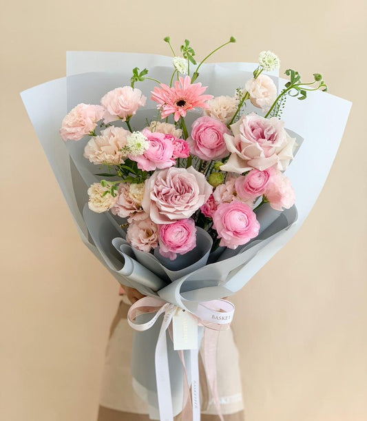 Pink and white fresh flower bouquet with roses, ranunculus, and gerbera daisy in grey-blue wrap