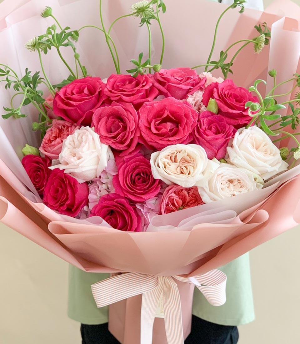 Pink and white rose bouquet with hydrangeas and green foliage, wrapped in pink paper with striped ribbon
