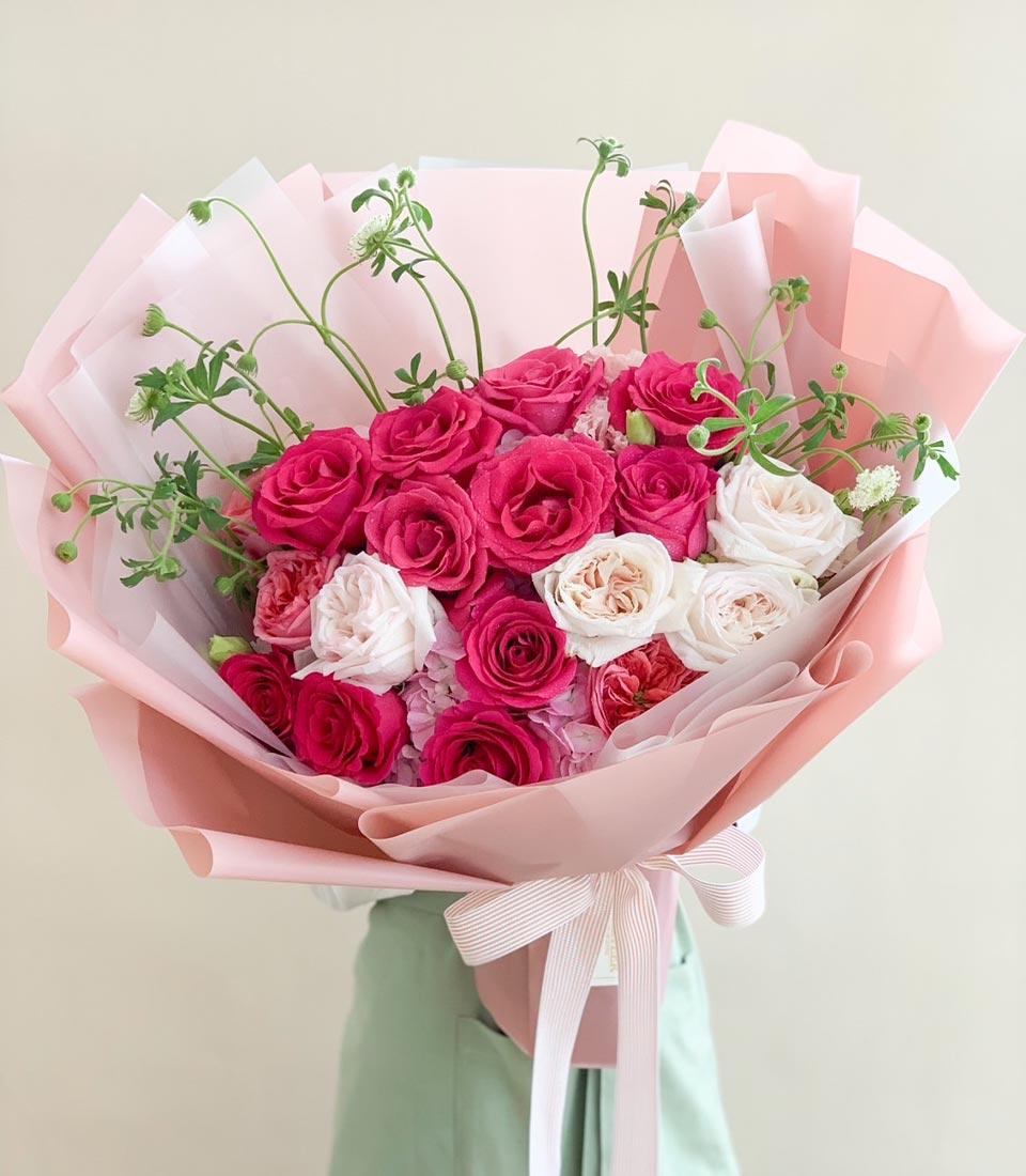 Fresh pink and white rose bouquet with green foliage, wrapped in translucent paper and pink striped ribbon