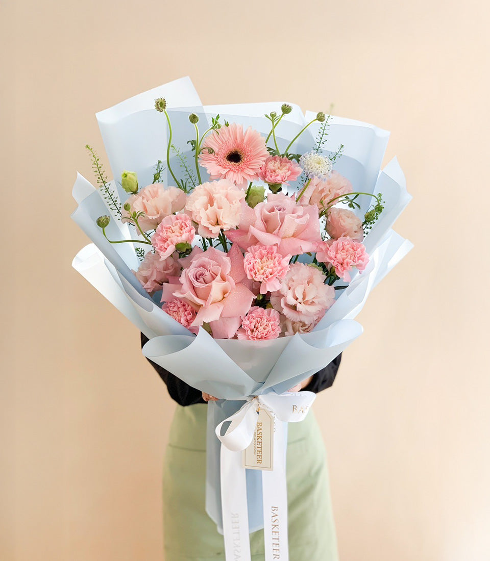 Blush pink rose and carnation bouquet wrapped in light blue paper with white ribbon
