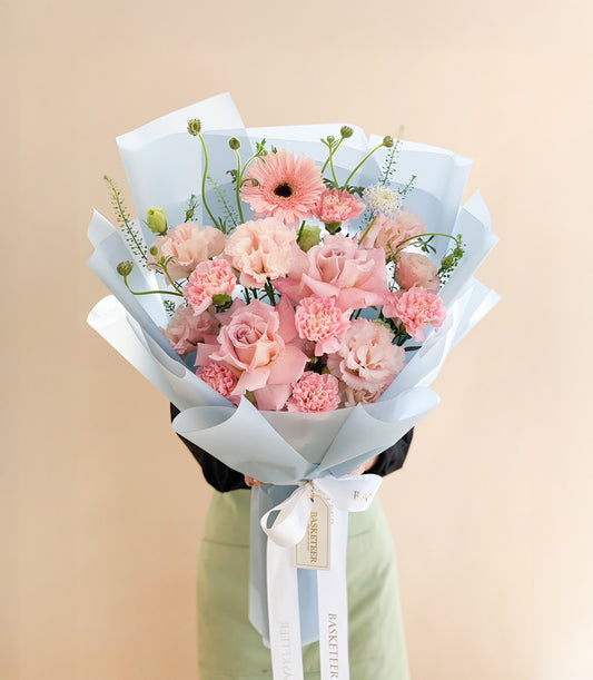 Blush pink rose and carnation bouquet wrapped in light blue paper with white ribbon
