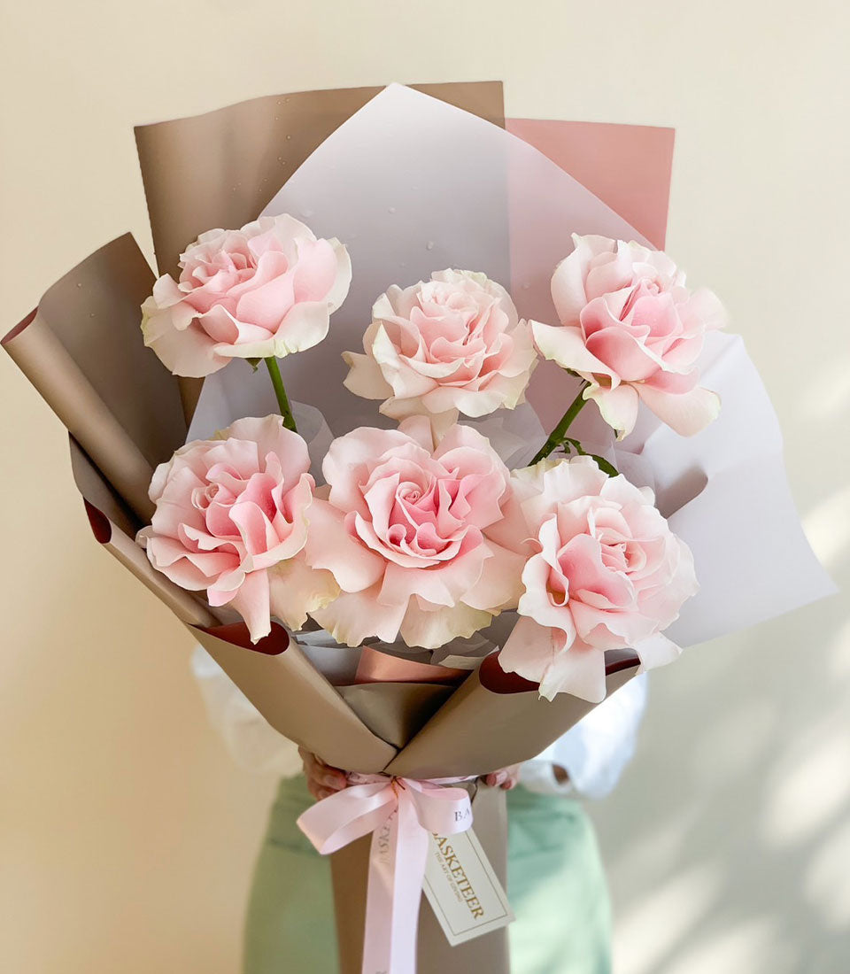Soft pink rose bouquet with delicate petals, wrapped in layered paper and pink satin ribbon for anniversaries