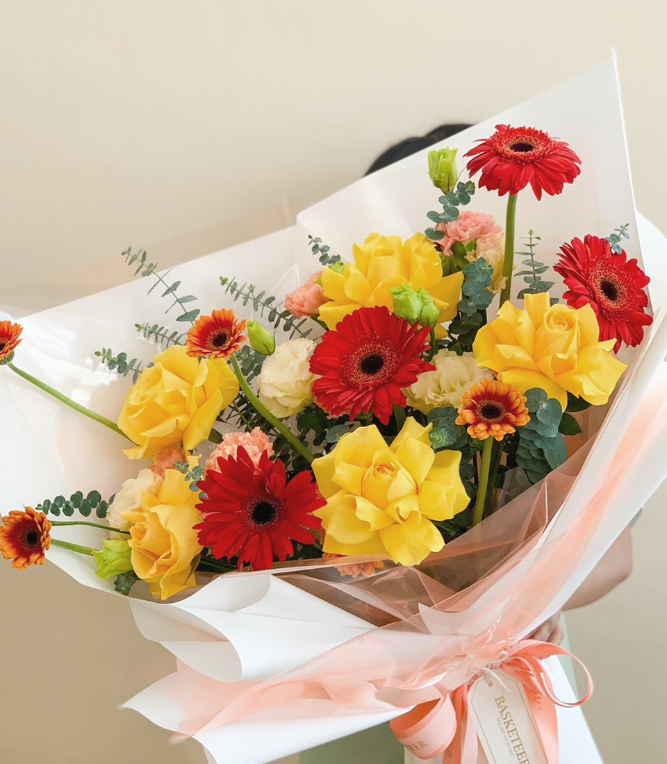 Radiance of Happiness Bouquet with red gerbera daisies, yellow roses, and pink carnations wrapped in peach paper