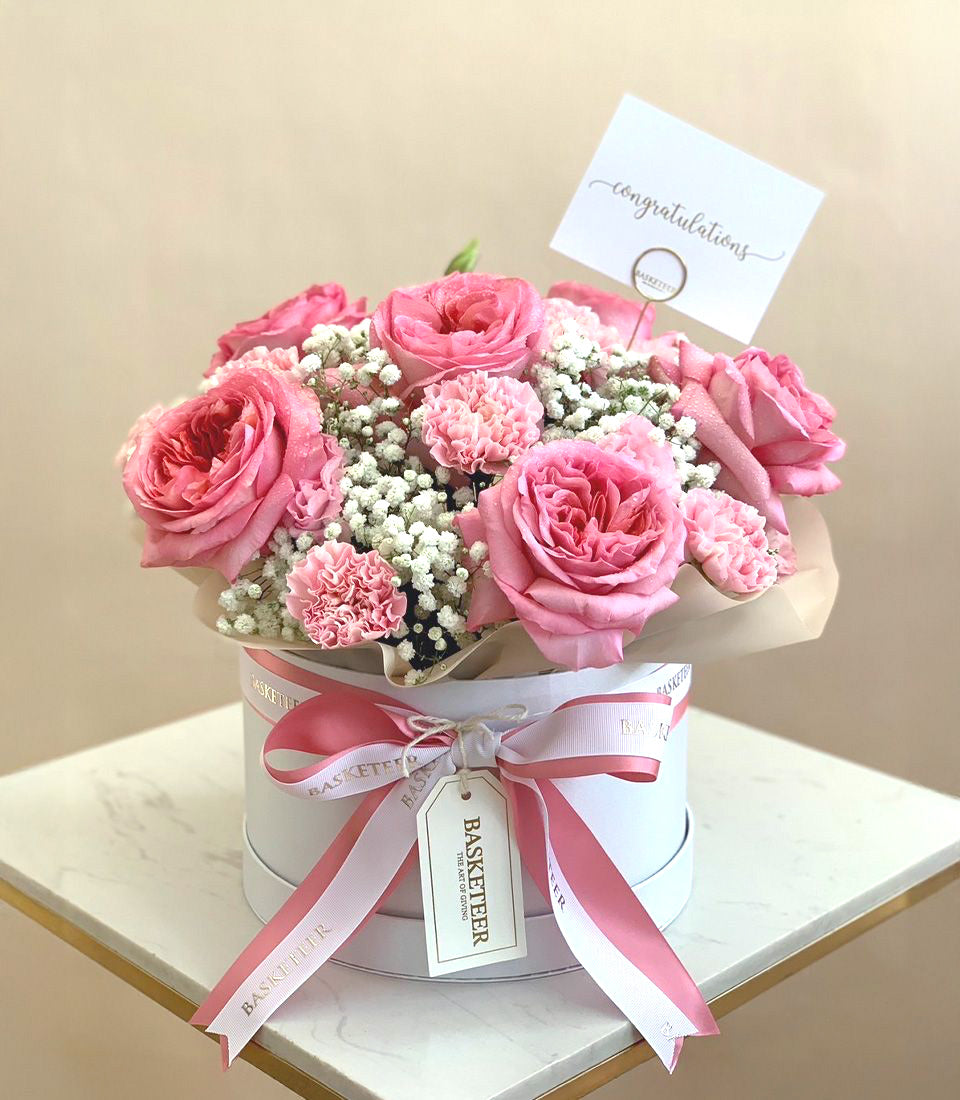 Blush pink roses and carnations in white hatbox with striped ribbon, congratulations flower gift