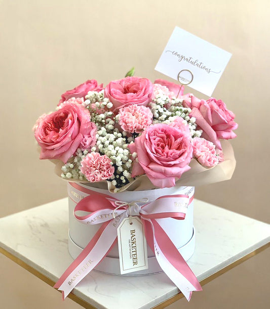 Blush pink roses and carnations in white hatbox with striped ribbon, congratulations flower gift
