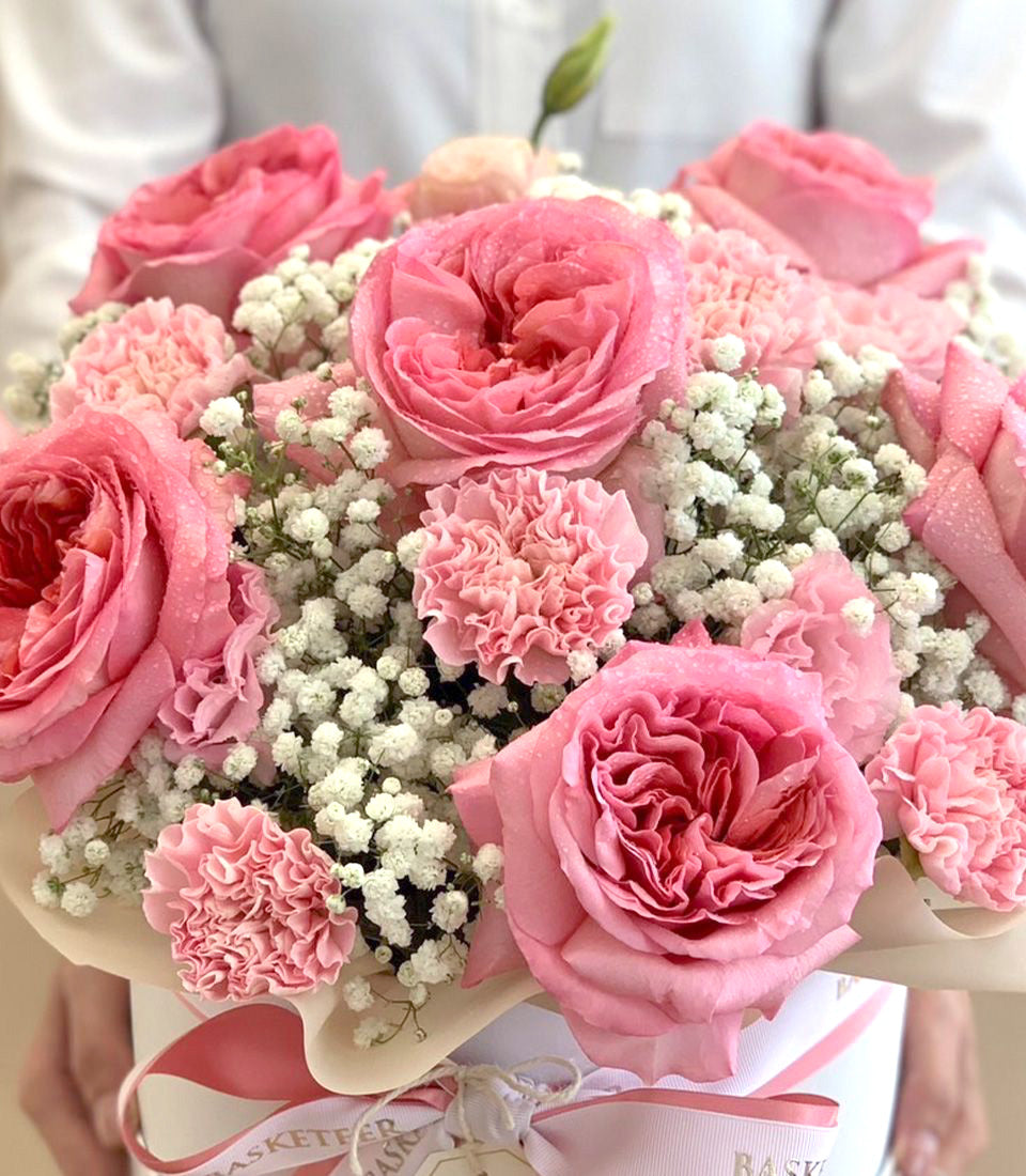 Blush pink roses and carnations with baby's breath in white hatbox with striped ribbon
