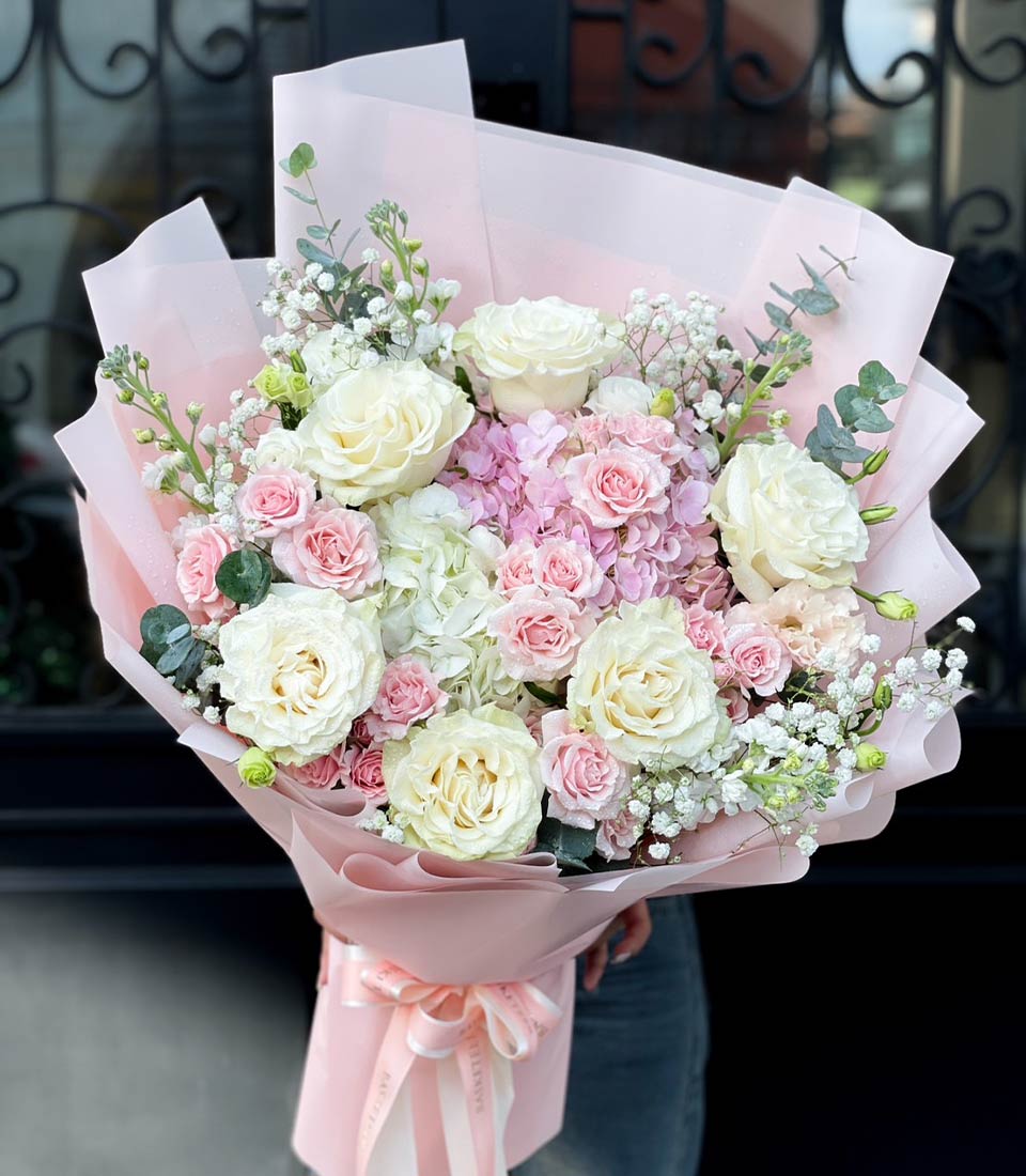 Pink and white rose bouquet with hydrangeas, baby's breath, and eucalyptus wrapped in light pink paper