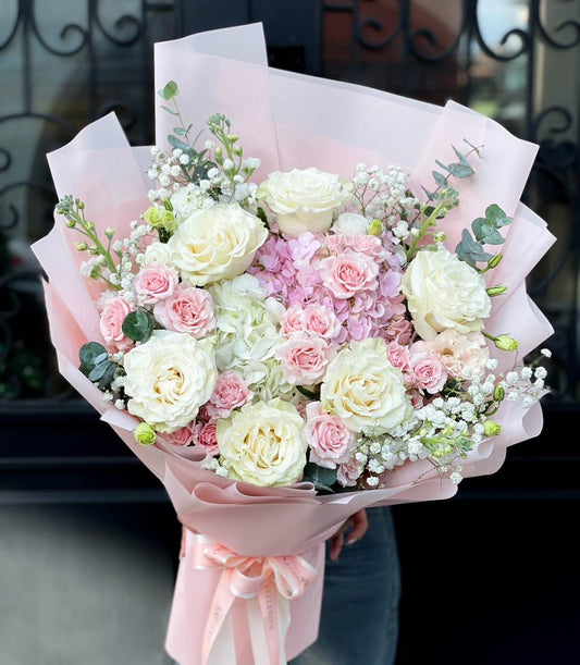 Pink and white rose bouquet with hydrangeas, baby's breath, and eucalyptus wrapped in light pink paper