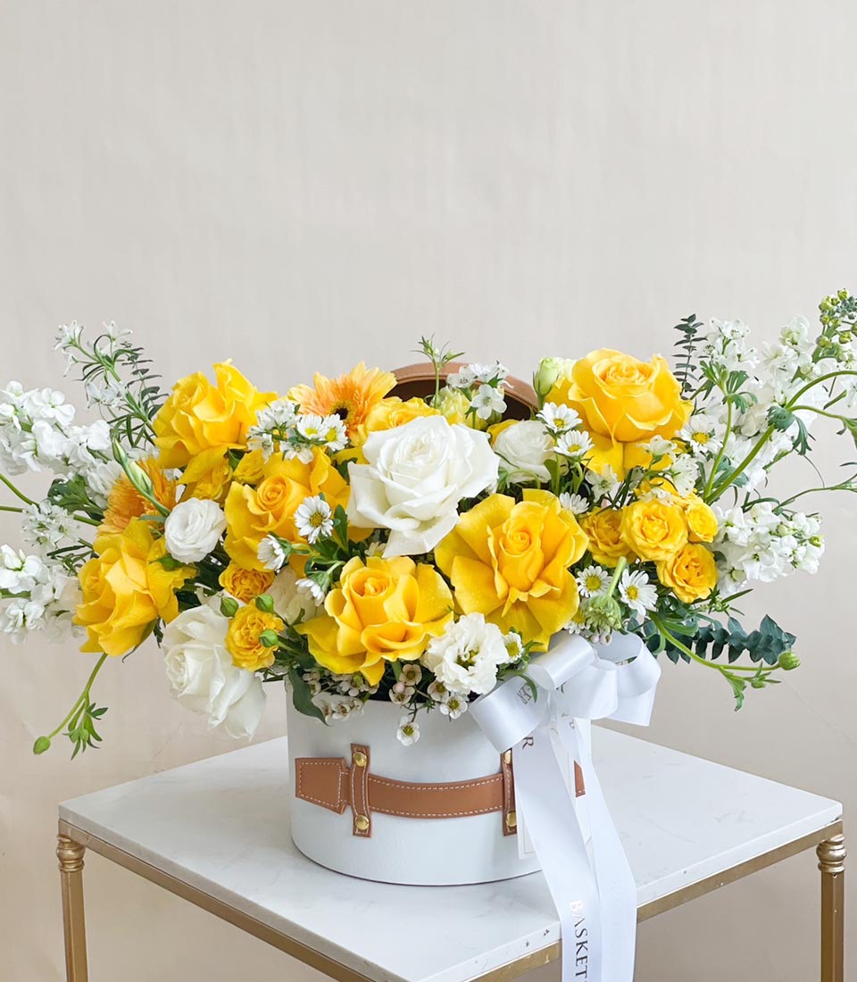 Yellow and white spring roses with gerbera daisies in luxury white hatbox with leather straps