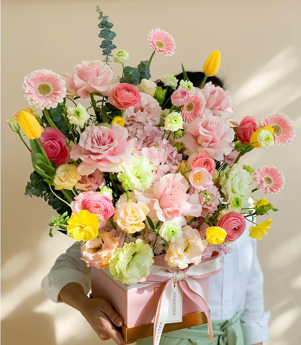 Vibrant spring flower arrangement in pink box with roses, gerberas, and ranunculus for graduation celebrations