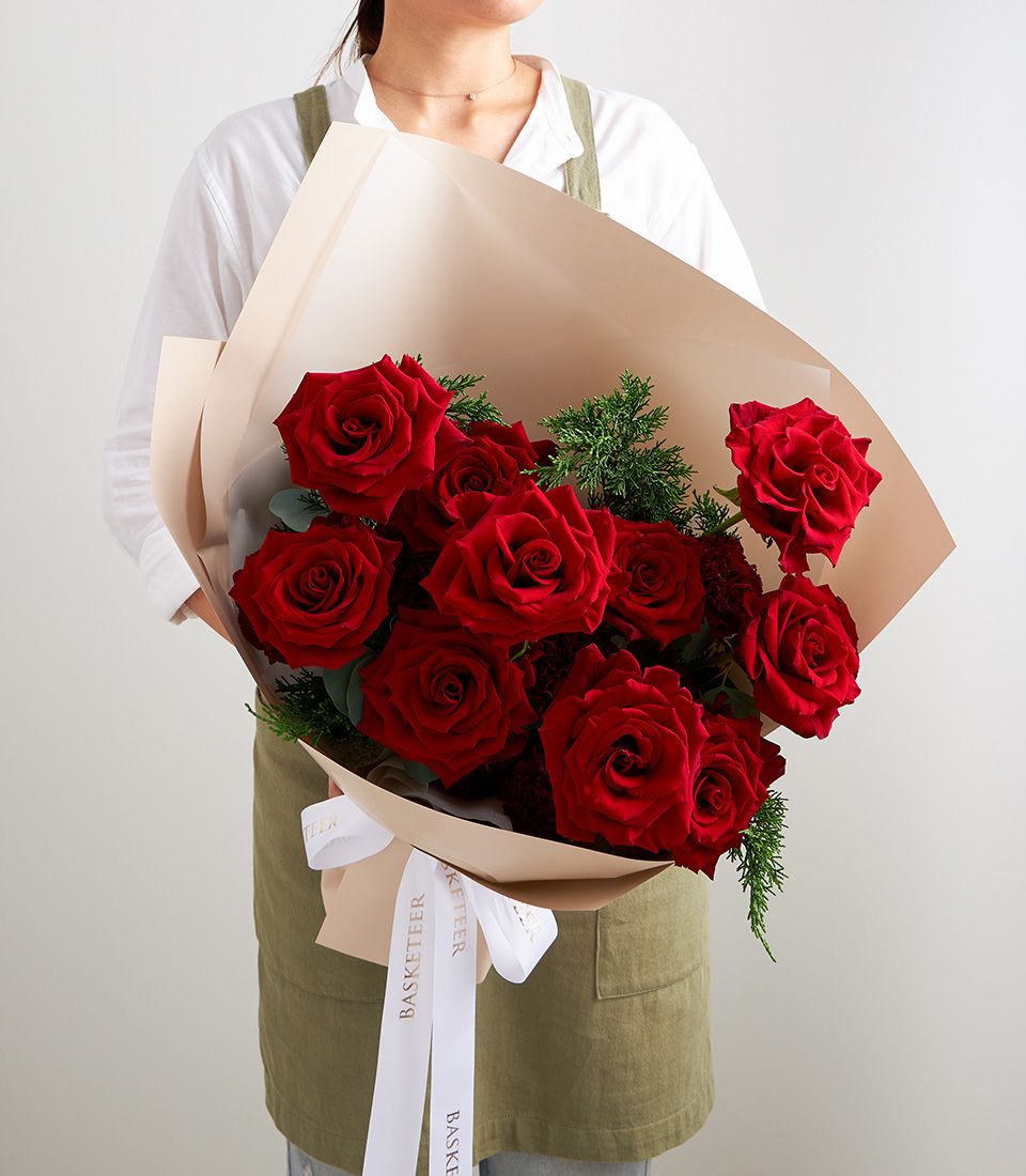 Lush red rose bouquet with cedar greenery and white ribbon bow, premium anniversary gift flowers