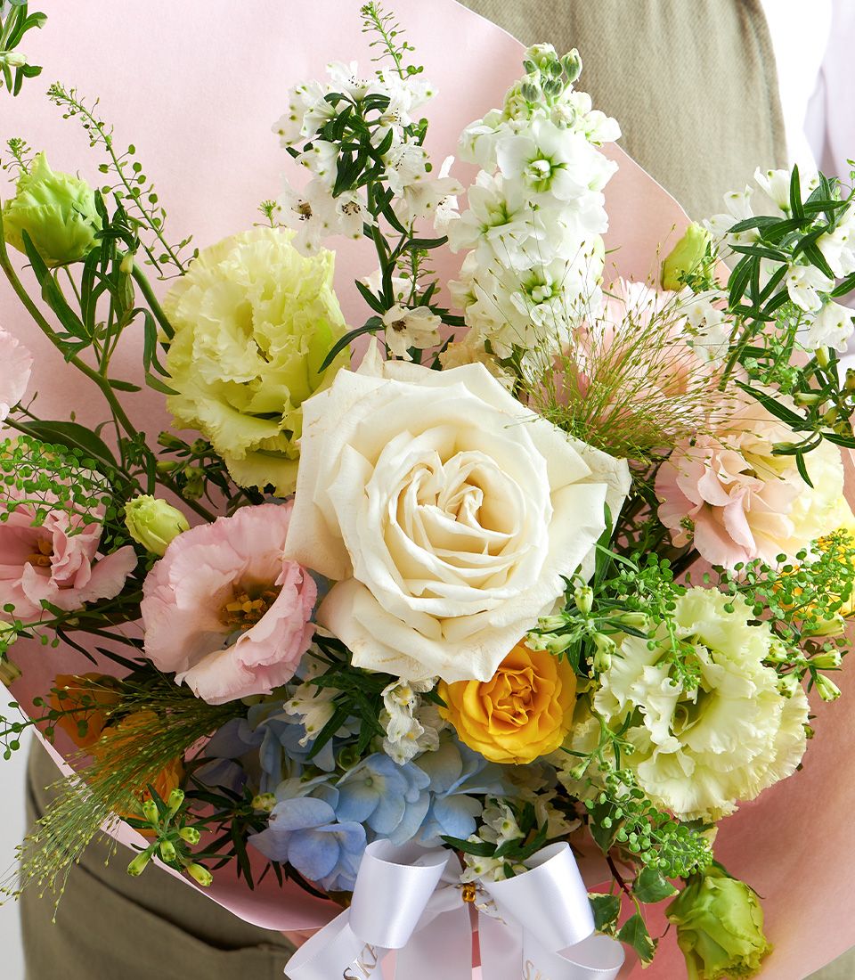 Pastel garden-style bouquet with cream rose, pale yellow Eustoma, and blue hydrangeas wrapped in pink paper