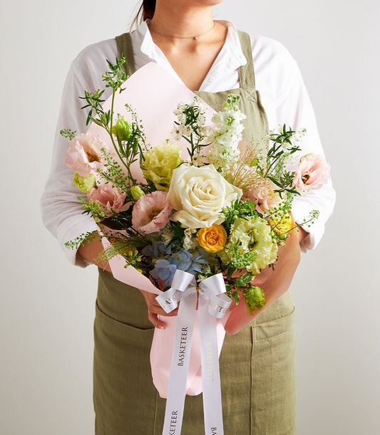 Pastel garden-style flower bouquet with cream roses, pink eustoma, and blue hydrangeas wrapped in light pink paper